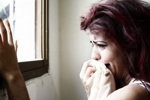 Photo of a woman crying into a cloth and looking out of a window