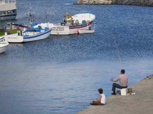 Photo of a man fishing on a beach with a boy sitting near him